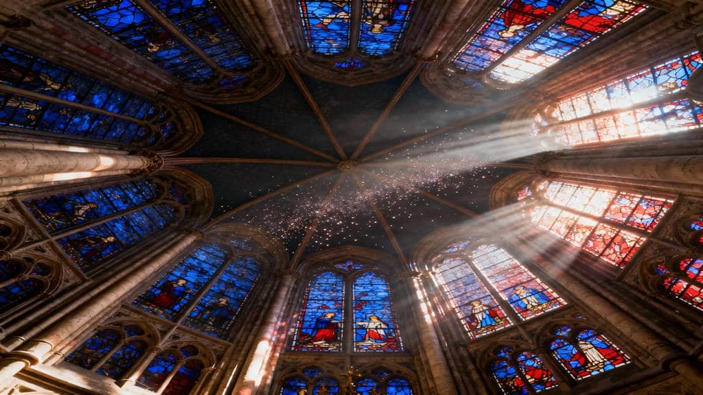 Low-angle view of the soaring stained-glass windows inside Sainte-Chapelle, with vibrant sunbeams of red and blue light cutting through the air and illuminating the Gothic interior.