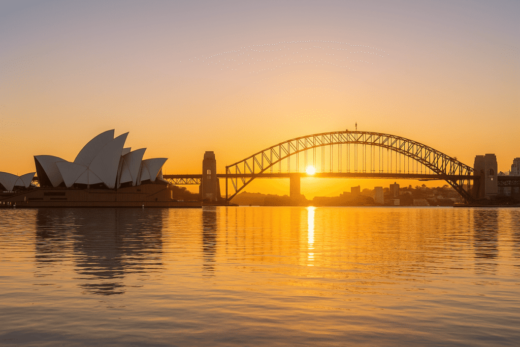 Sydney Opera House and Harbour Bridge at sunrise reflected in calm harbour waters.